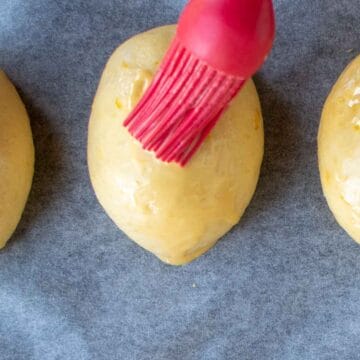 Yellow dough ball being brush with egg wash.