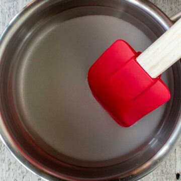Sugar and water being stirred in a pan with a red spatula.
