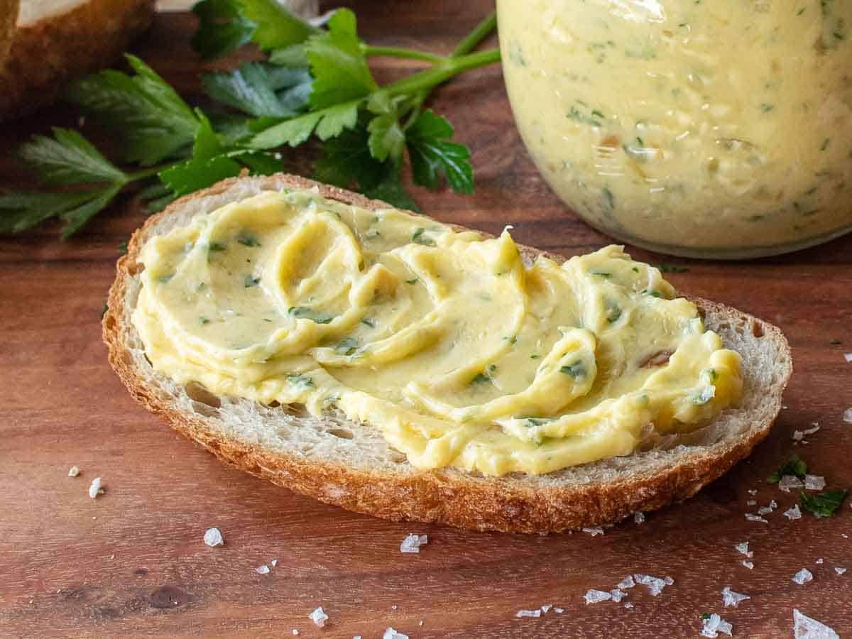 Softened butter with green herb flecks spread on an oblong slice of bread.