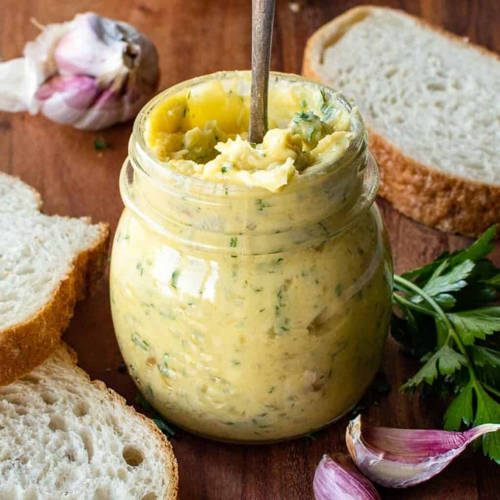 Roasted garlic butter in a jar with a spoon inserted.