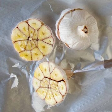 Two whole garlic bulbs cut in half with one showing the inside cross section.