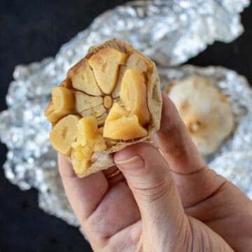 Cross section of roasted garlic being squeeze with fingers.