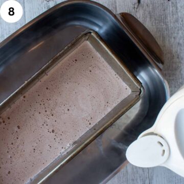 Light brown creamy liquid in a loaf pan in a large baking pan with water being poured in.