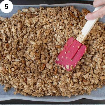 Brownish oat mixture on a baking sheet pressed by red spatula.