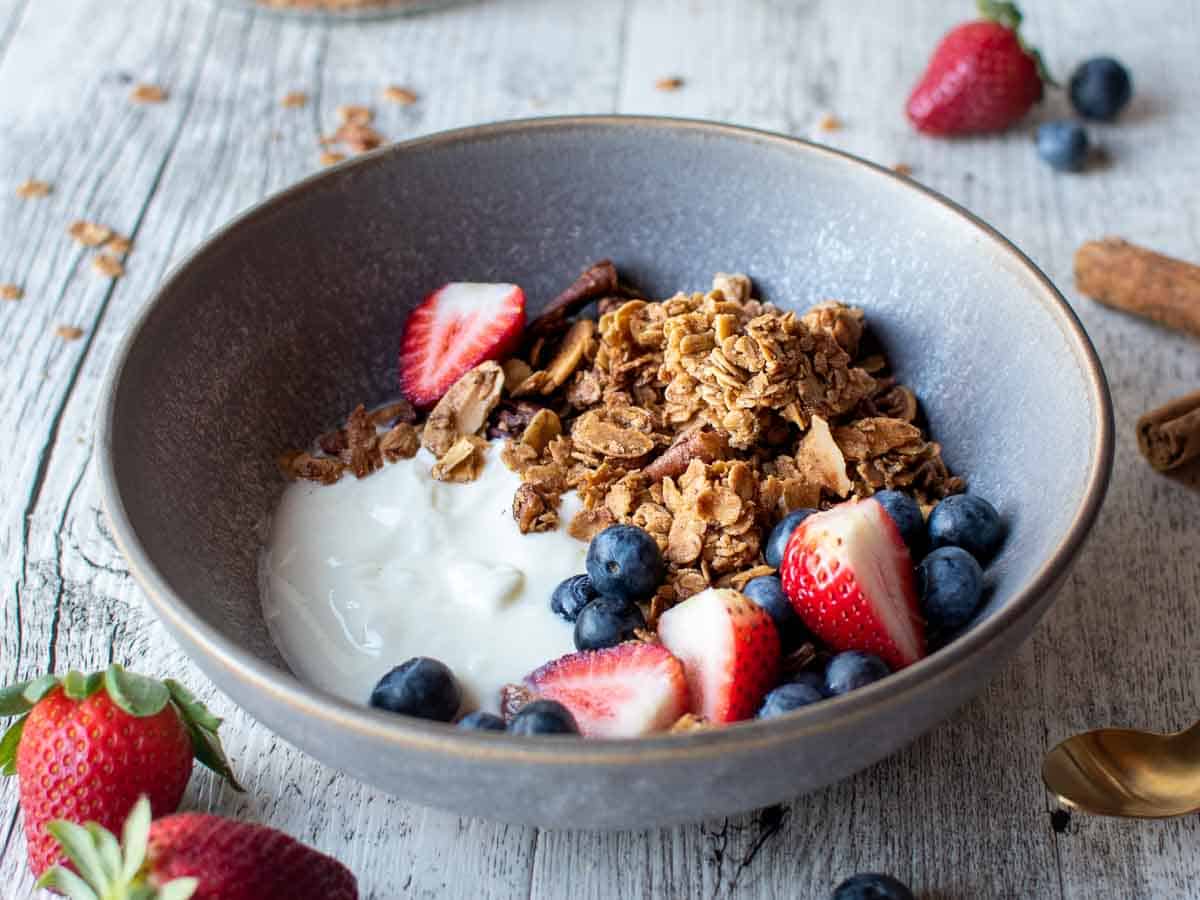 Grey bowl filled with toasted granola, white yogurt and berries.