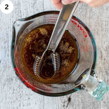 Syrup and oil in a glass jug with a small whisk viewed from above.