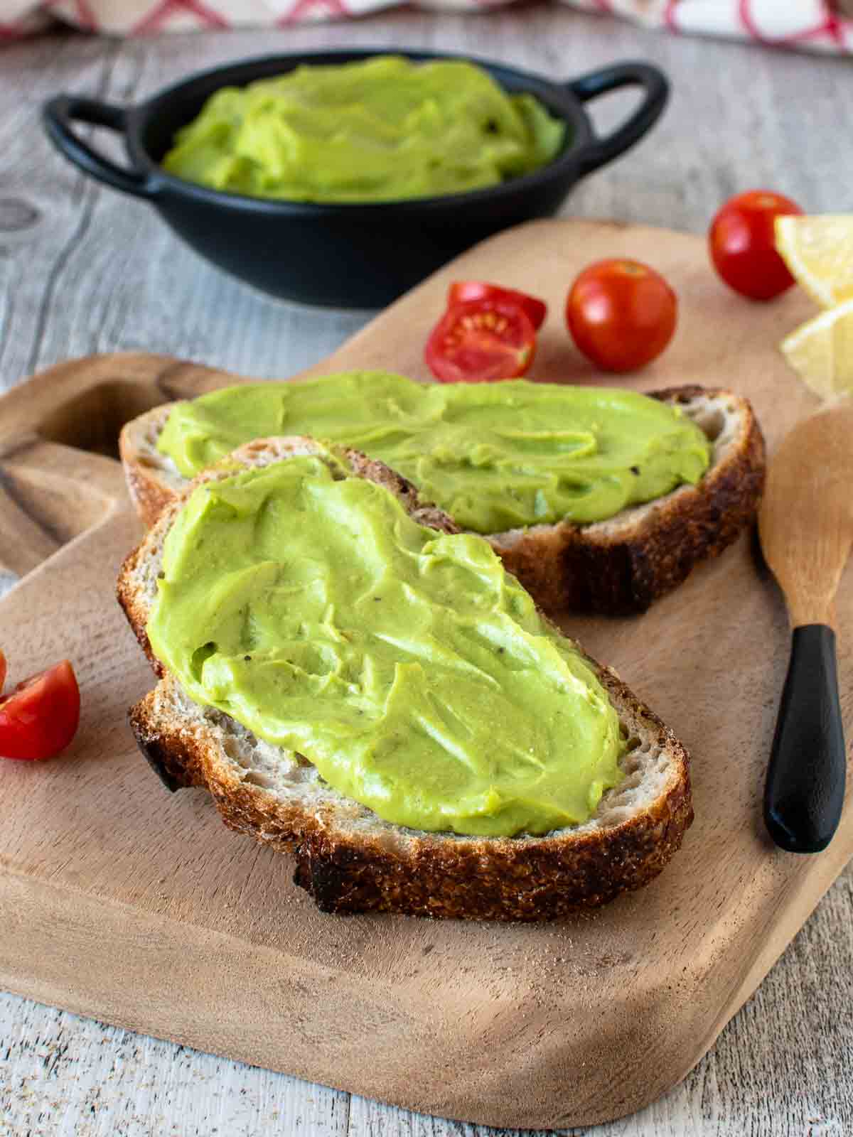 Avocado Spread on two slices of sourdough bread, cherry tomatoes and more spread in background.