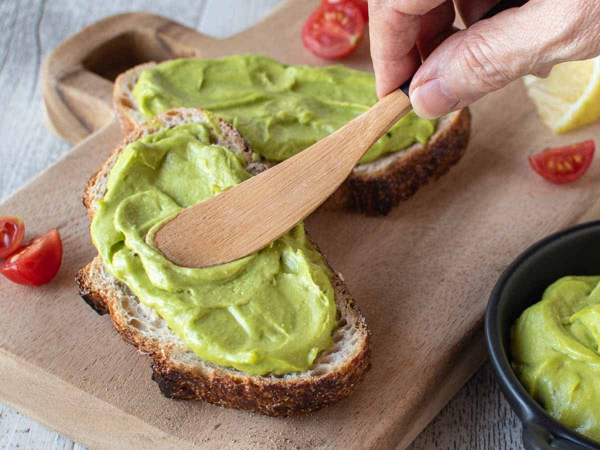 Green smooth dip being spread onto sourdough bread.