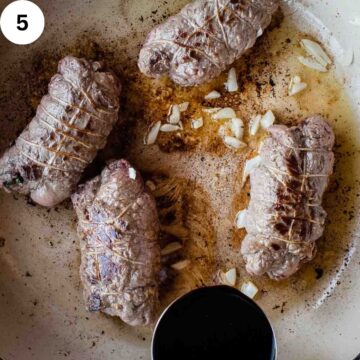 Red wine being added to browned beef rolls in a pan.