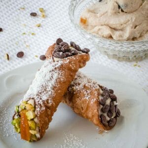 Two filled cannoli resting on each other on a white plate.