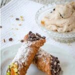 Two filled cannoli resting on each other on a white plate.