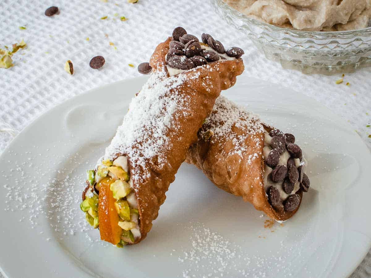 Two filled cannoli resting on each other on a white plate.