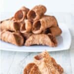 Two Cannoli Shells in front of a white plate piled high with cannoli shells.