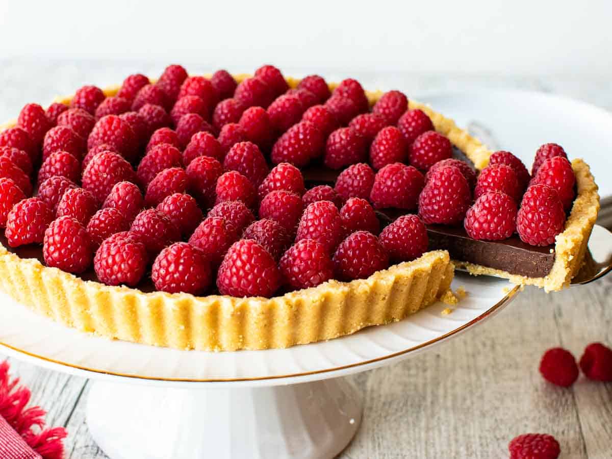 Close up of chocolate tart with raspberry on top with a wedge cut.