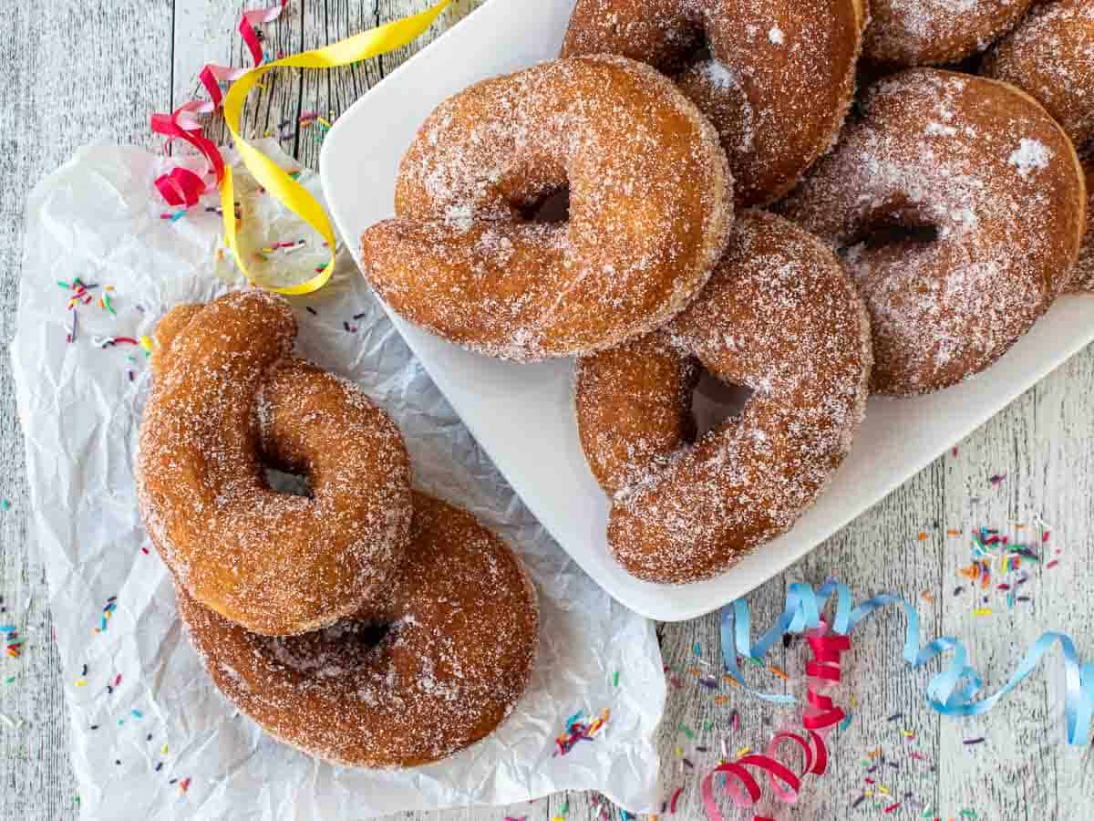 Overhead view of Italian donuts on a white rectangle plate with two on the side on kitchen towel.