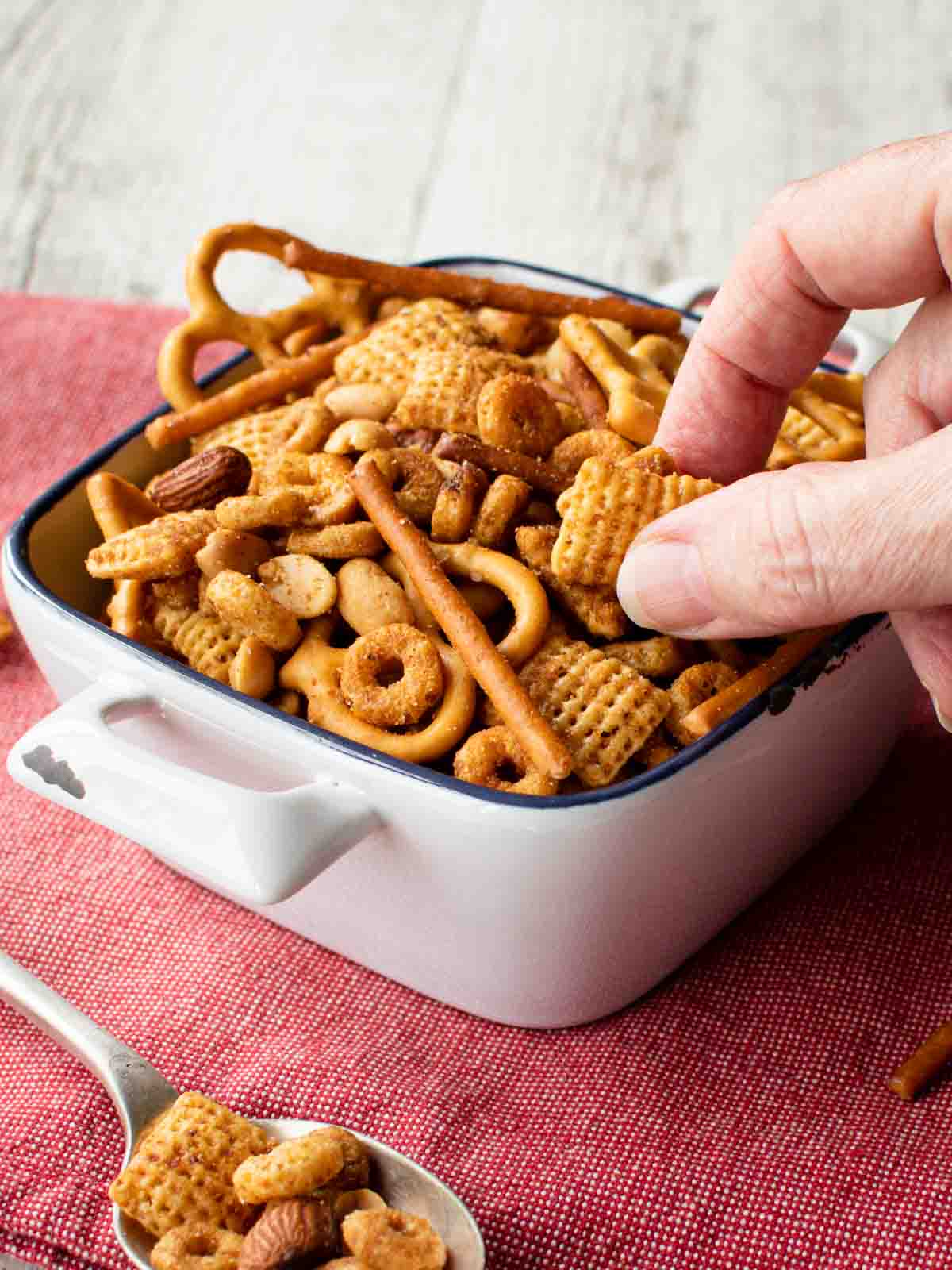 Nuts and Bolts in a white square ceramic bowl with fingers picking up some.