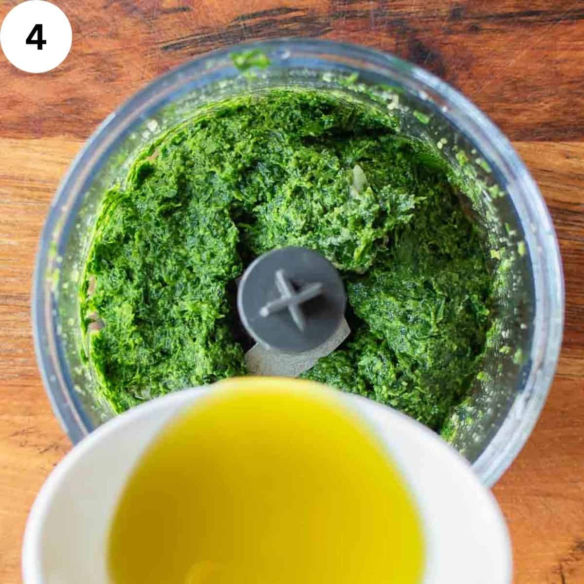 Oil being poured into a parsley paste in a food processor.