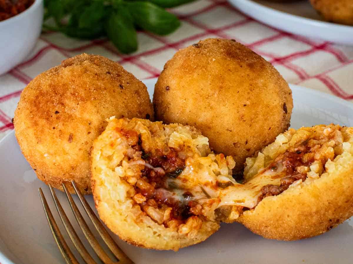 Close up of halved arancini with two whole arancini in the background.