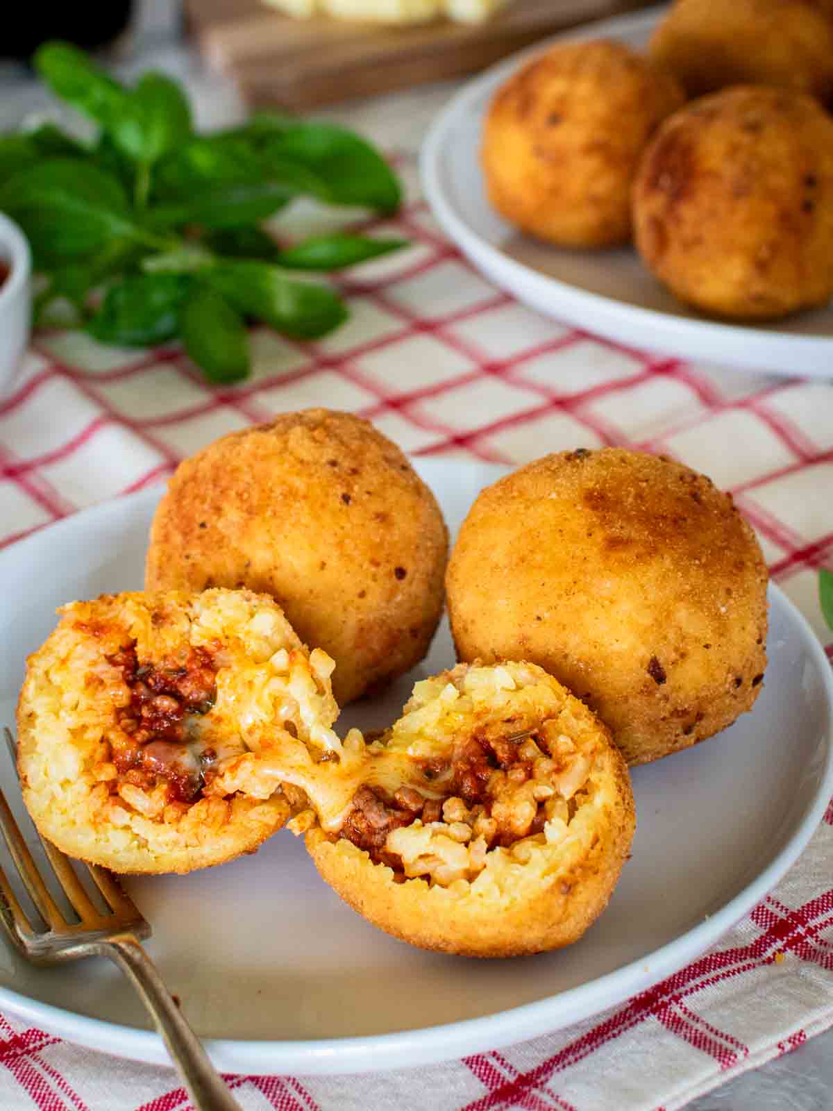 Three Italian Rice Balls on a plate with one ball split in half.