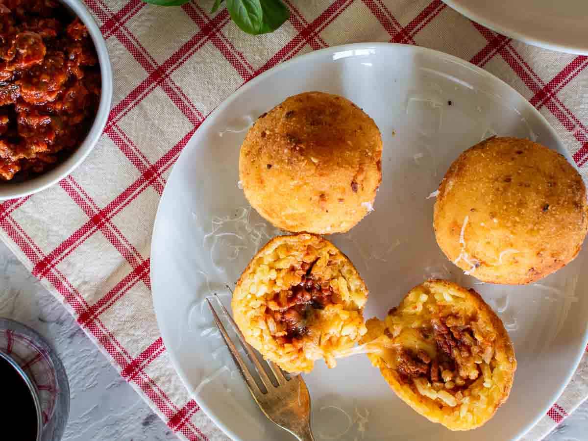 Sicilian rice balls on a plate with one cut in half viewed from above.