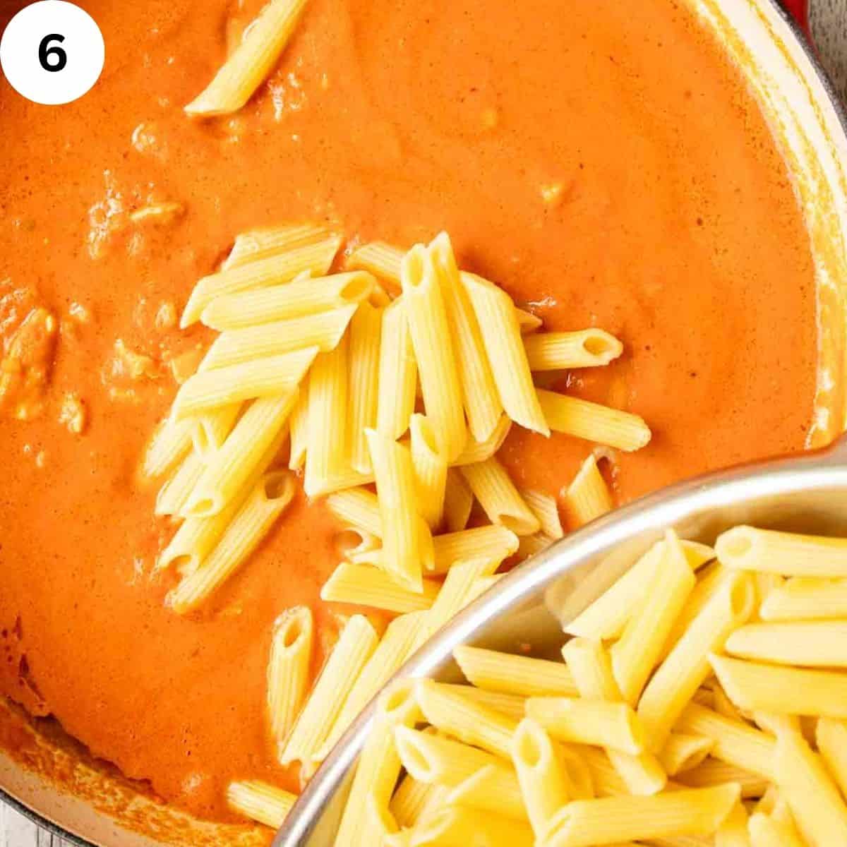 Cooked penne pasta being added to creamy tomato sauce.