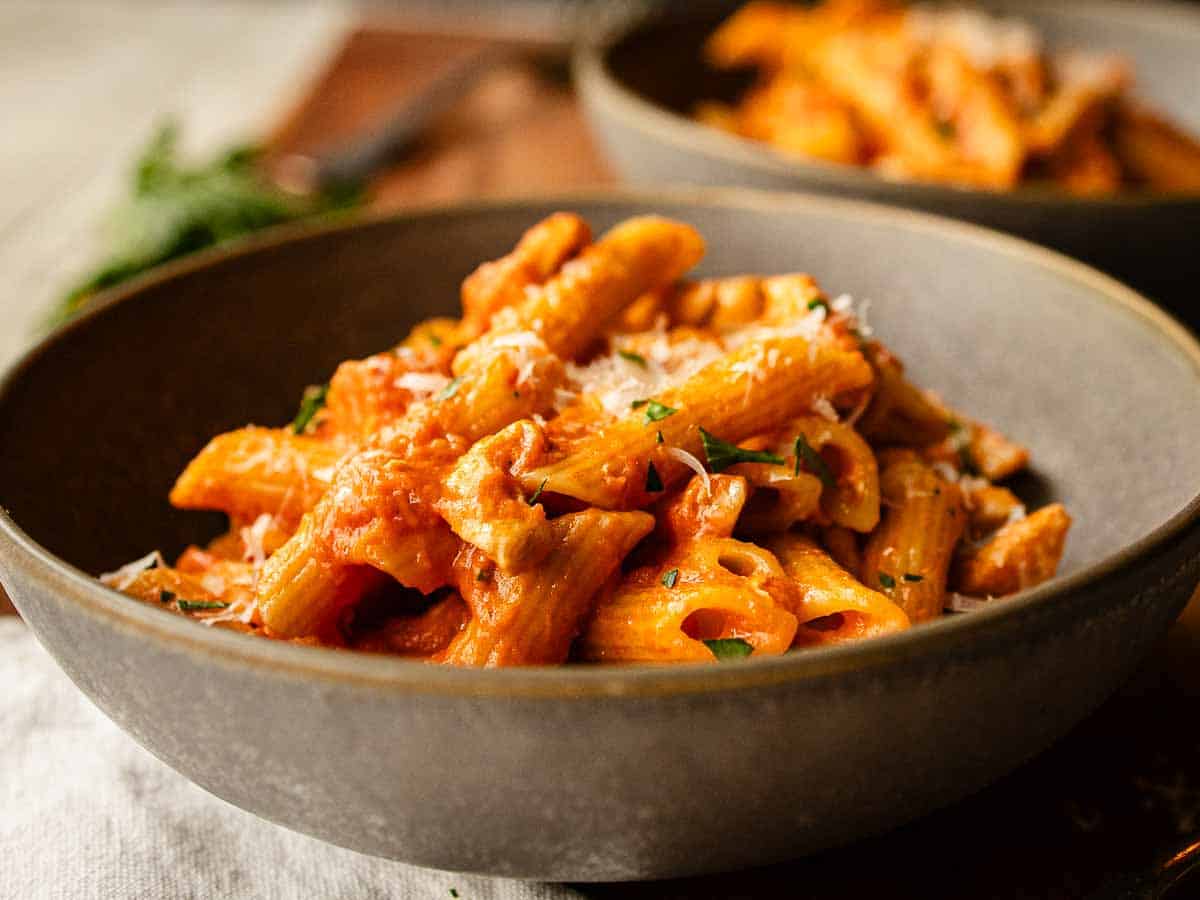 Close up of penne pasta coated in creamy tomato sauce in a bowl.