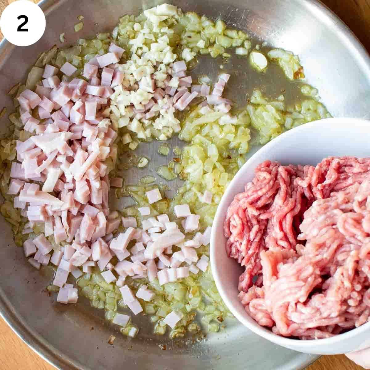 Ground meat being added to sauteed onions and bacon in a pan.