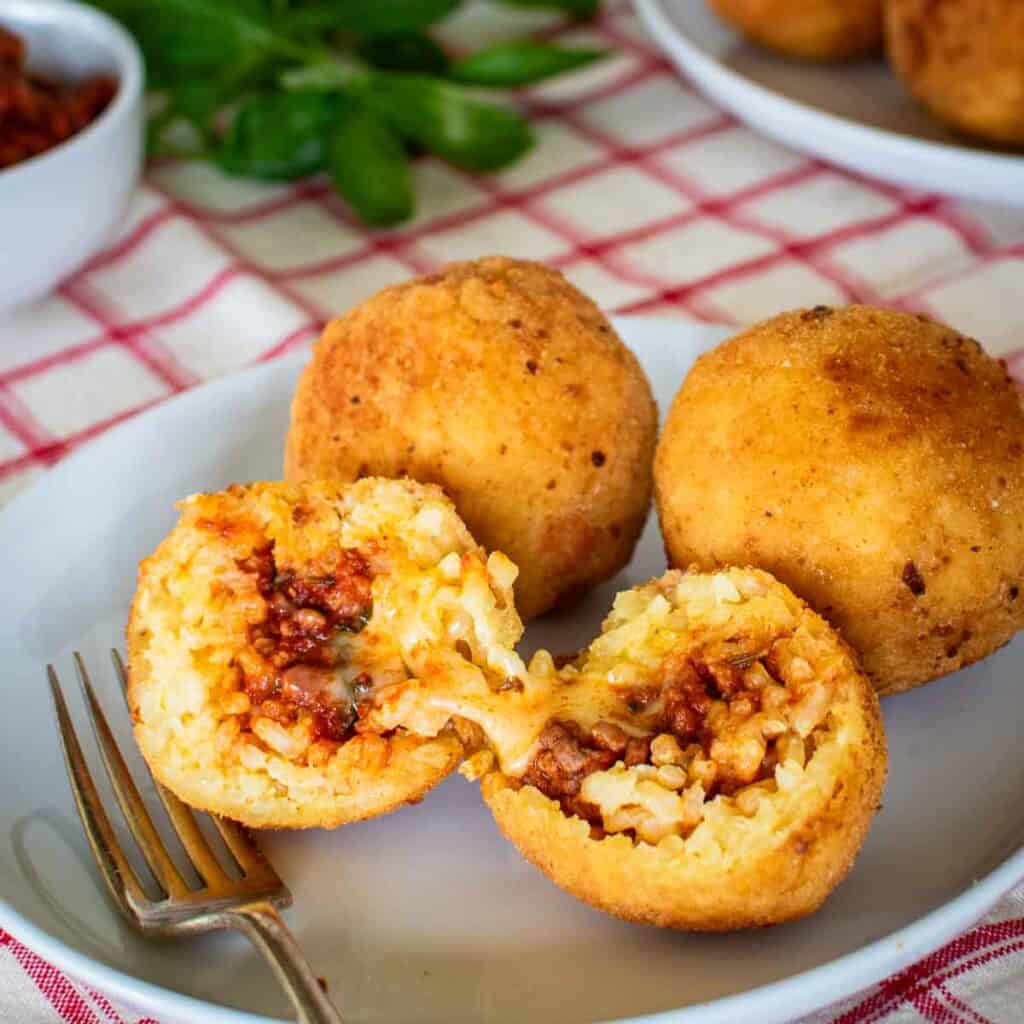 Three Italian Rice Balls on a plate with one ball split in half.