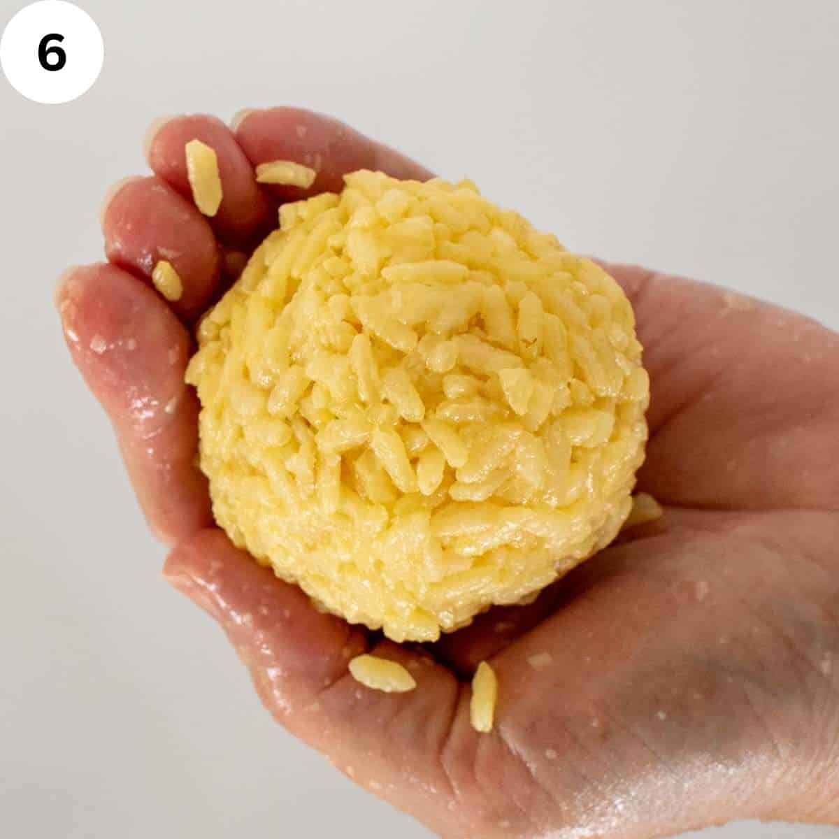 Ball of yellow rice held in the palm of a hand.