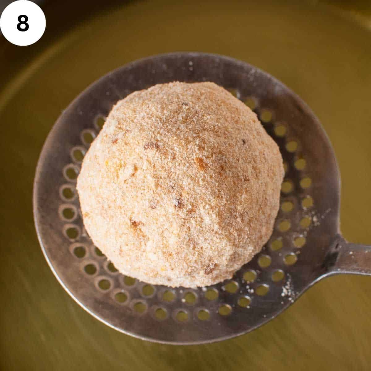 A bread crumb covered rice ball on a slotted spoon.