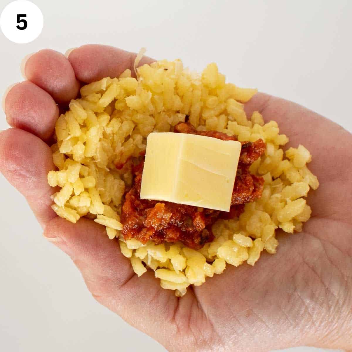 Rice flattened into the palm of hand, topped with meat sauce and cube of cheese.