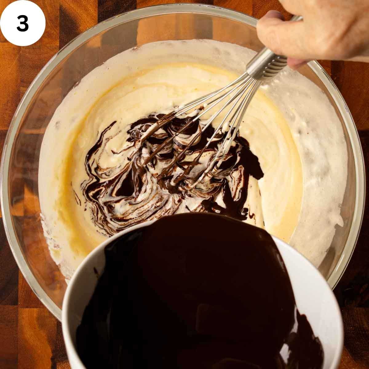 Melted chocolate being whisked into creamy yellow mixture.