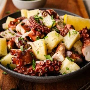 Octopus salad in a bowl on a wooden board.