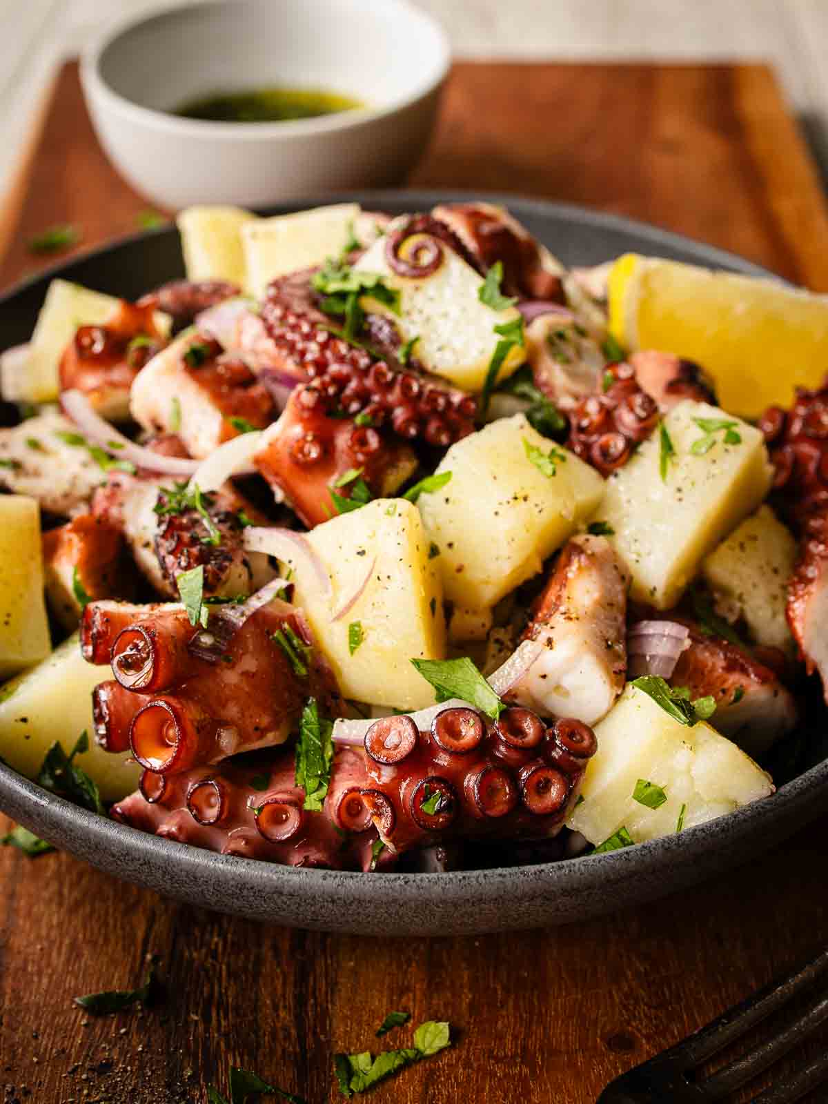 Octopus salad in a bowl on a wooden board.