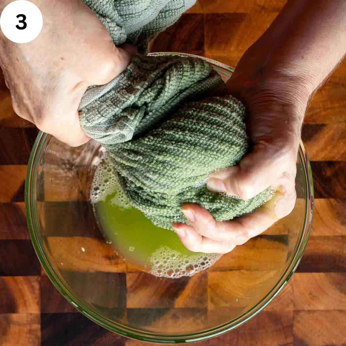 A kitchen towel being squeezed above a bowl filled with green liquid.