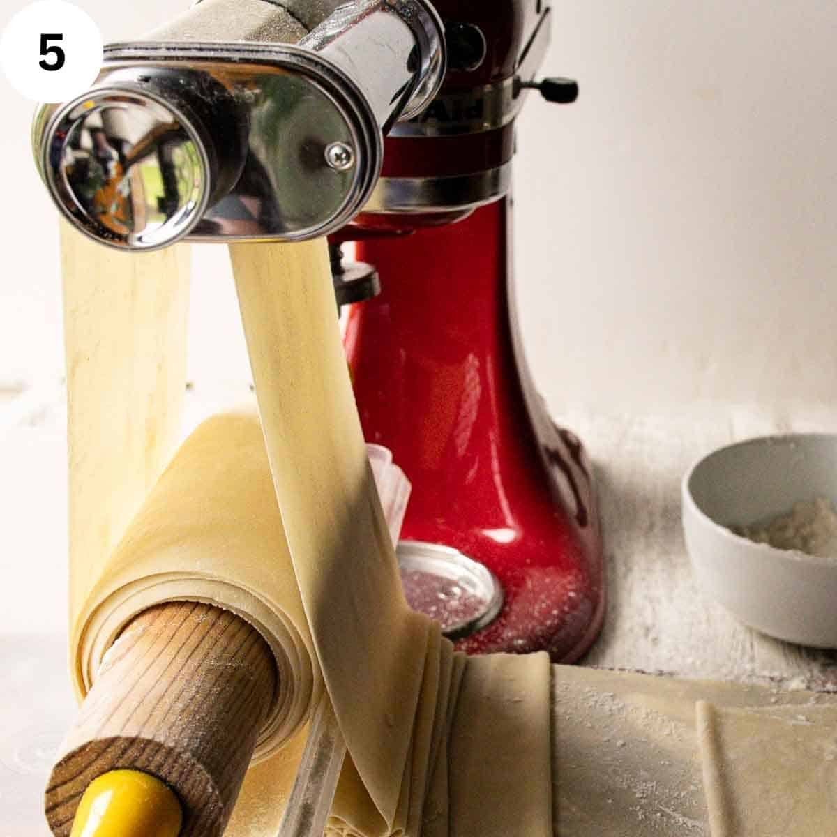 Thin dough being rolled through pasta machine rollers.