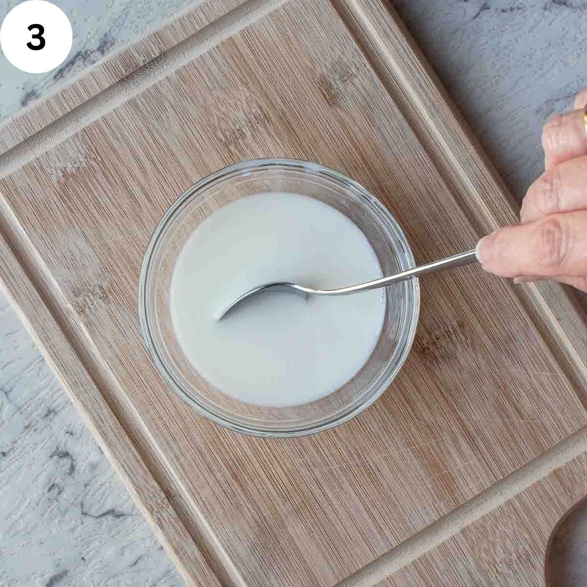 Stirring white liquid in a small bowl with a teaspoon.