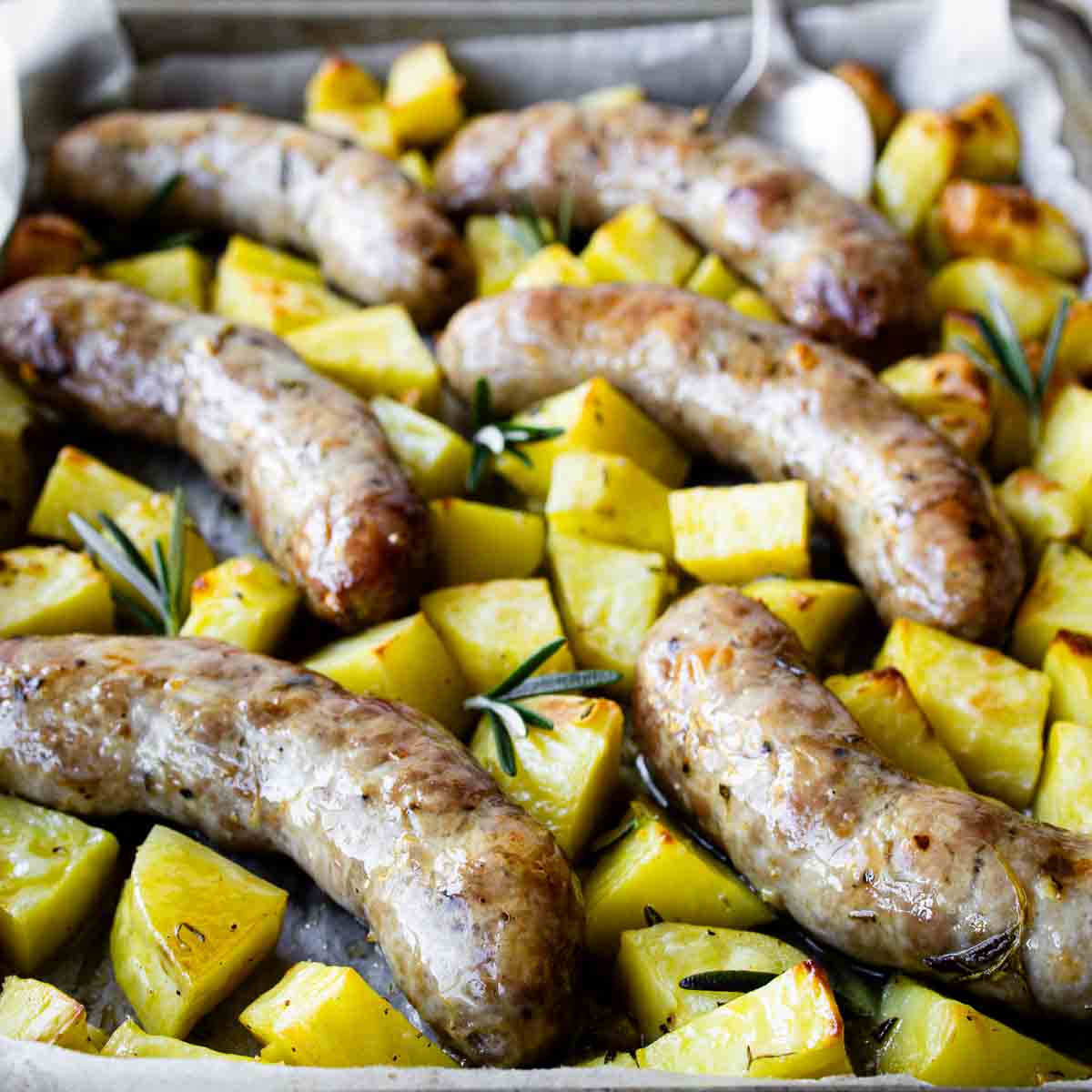 Baked Italian sausages and potatoes in a baking dish.