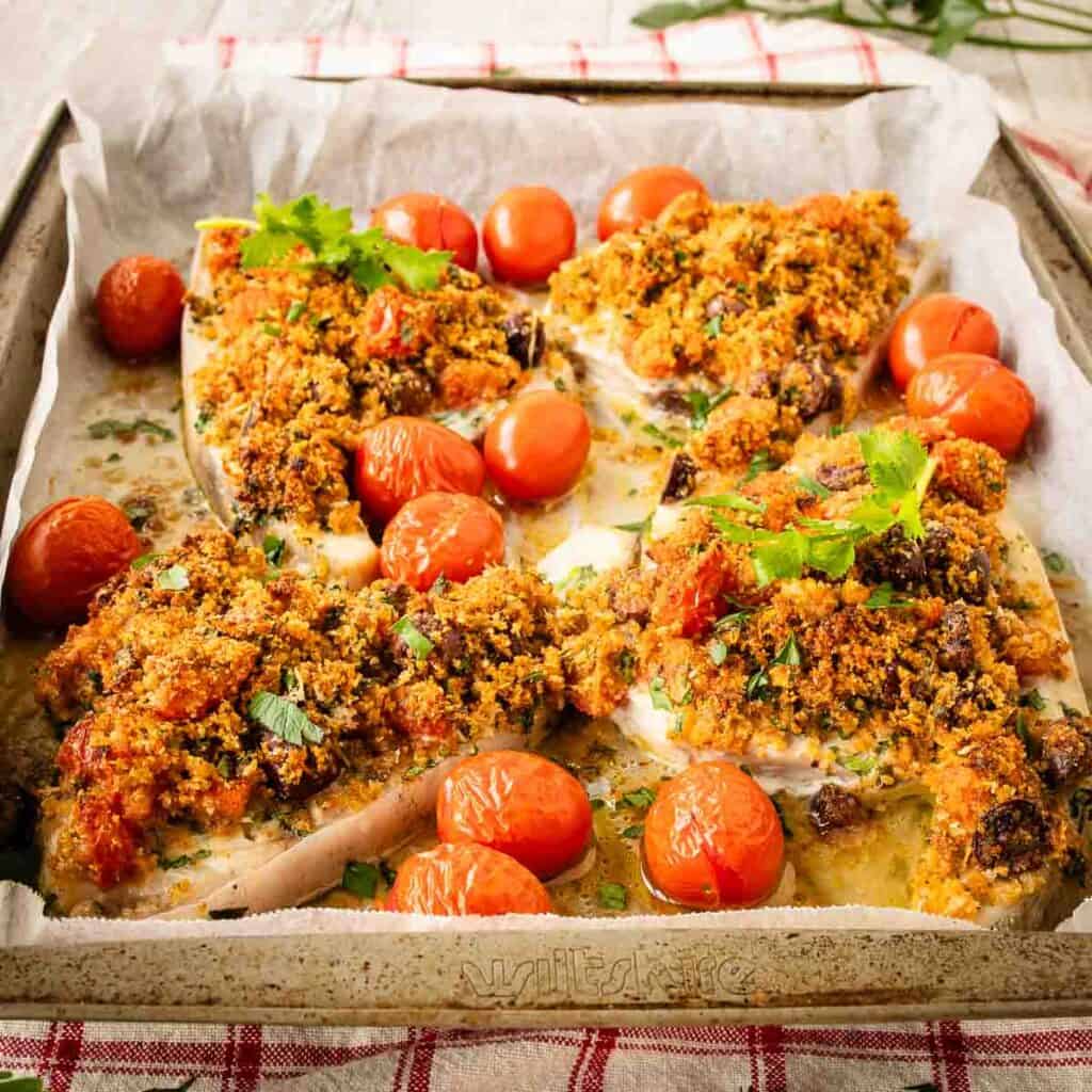 Baked Swordfish with a gratin topping surrounded by baked cherry tomatoes.