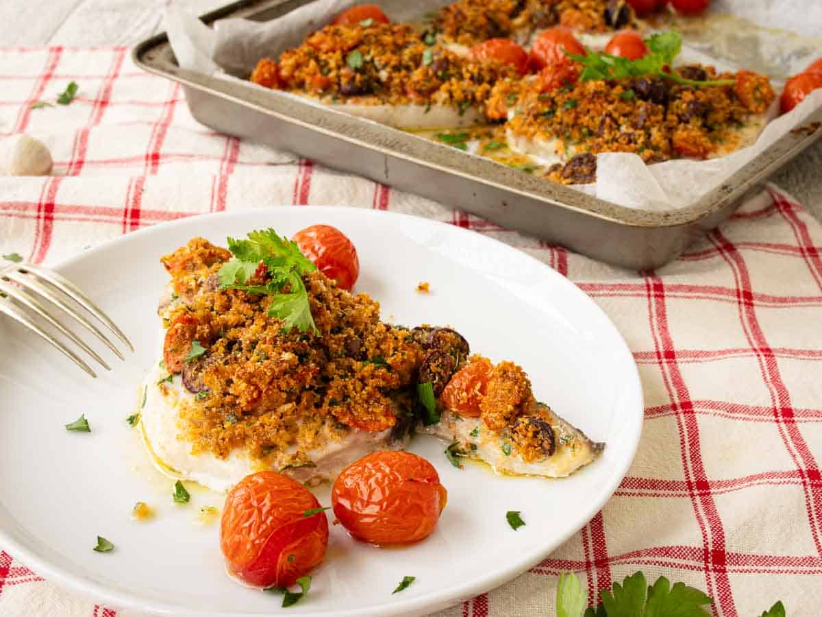 Swordfish topped with toasted breadcrumb topping on a round plate with baking pan at the rear.