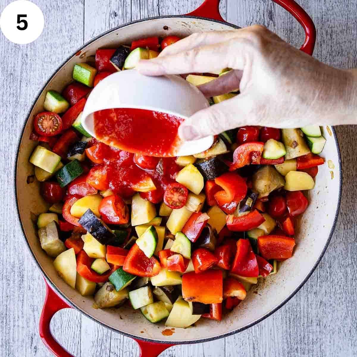 Pour tomato puree into a pan of sauteed mixed vegetables.