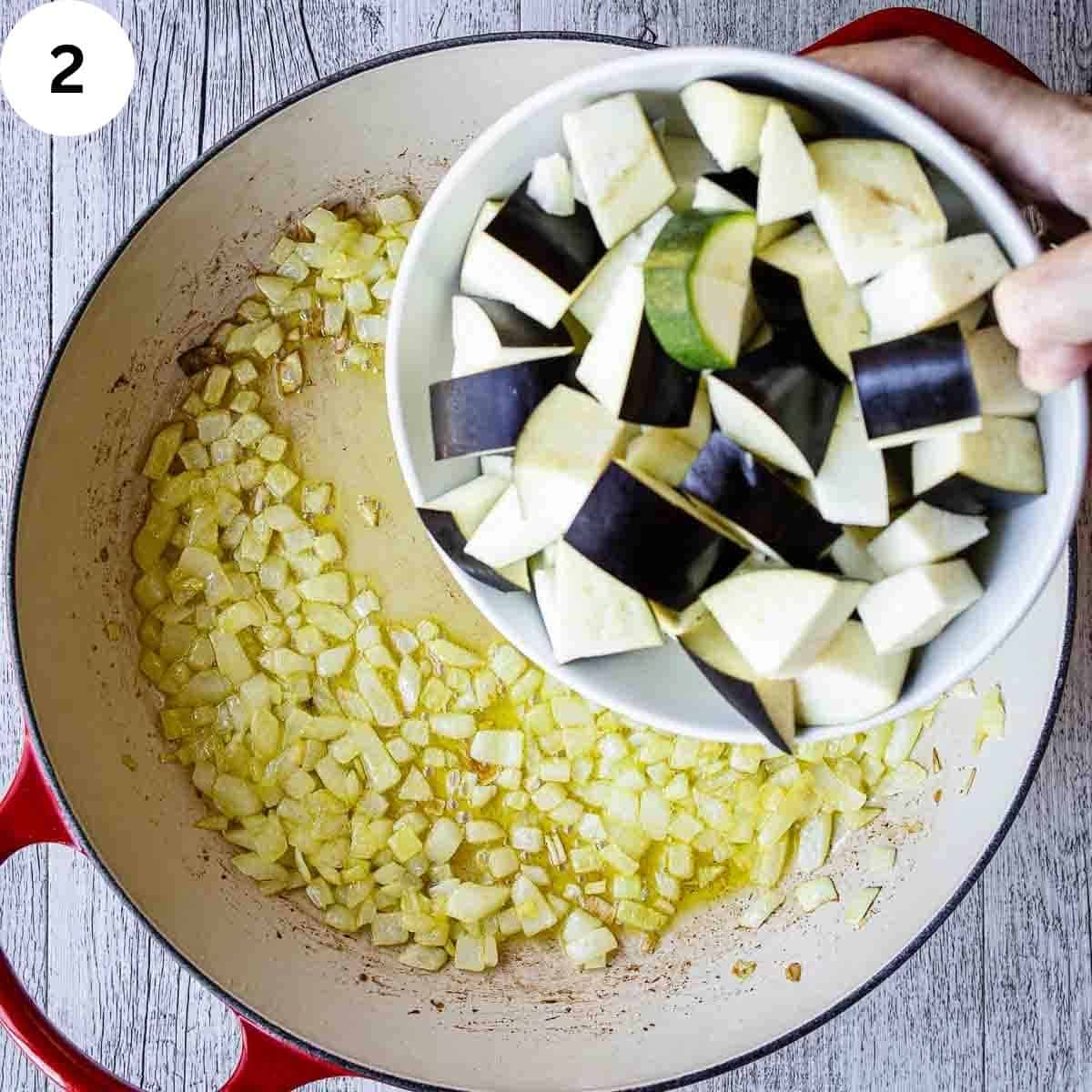Adding chopped eggplant to a round pan of sauteed chopped onions.