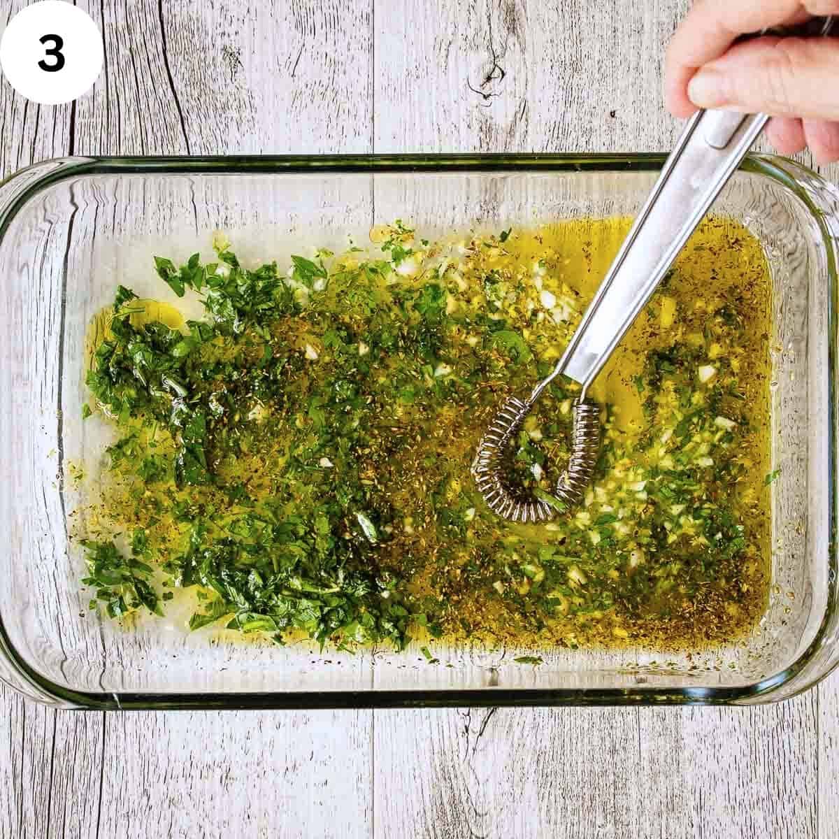 Whisking olive oil together with chopped herbs in an oblong dish.