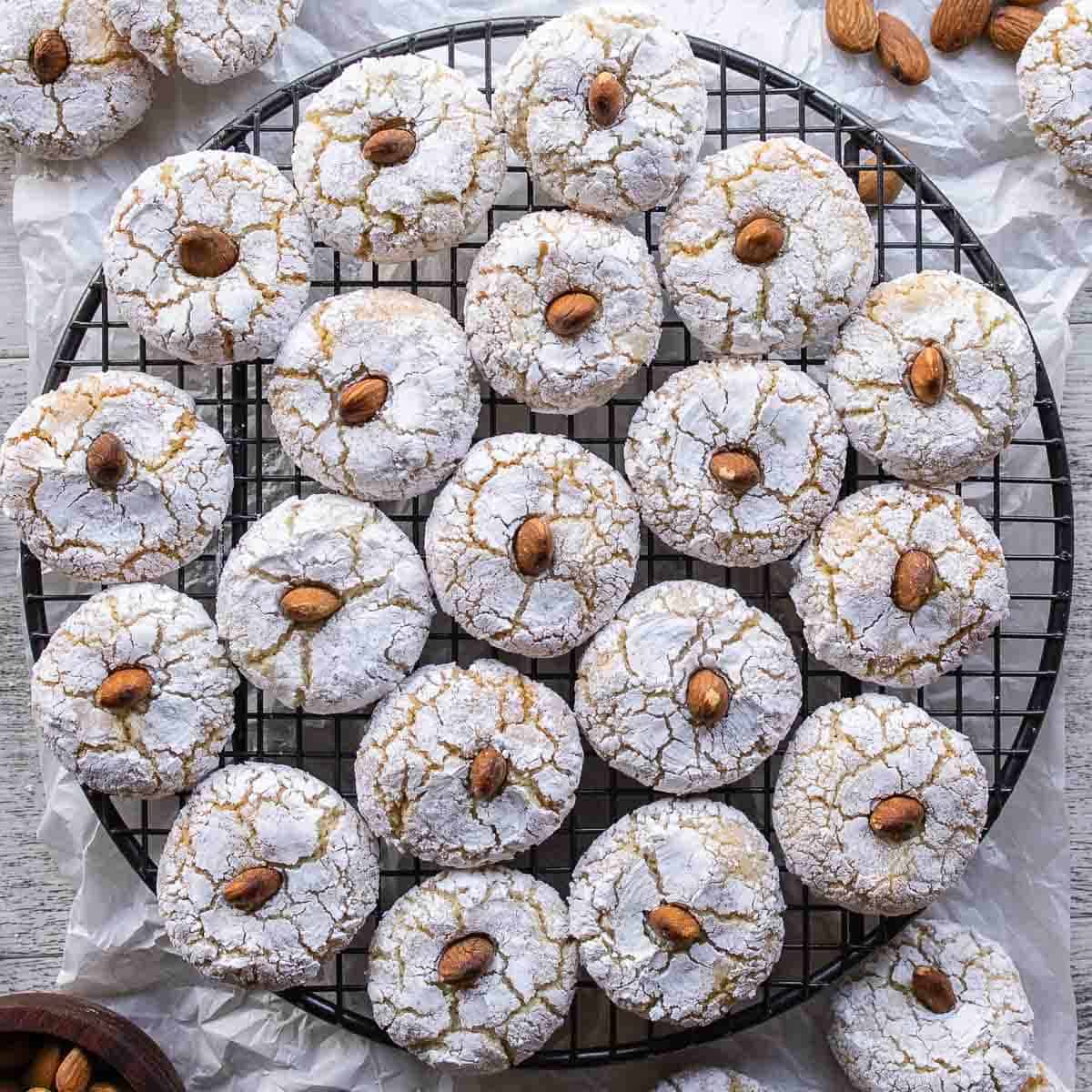 Amaretti Cookies on a round wire rack viewed from above. 3 cups (288 grams) ground almonds 3 egg whites 1 ¼ cup (250 grams) granulated white sugar 1 teaspoon almond extract Powdered sugar Almonds for decorating Prepare two baking sheets by lining them with parchment paper and preheat the oven to 350ºF/180°C. Combine the ground almonds with the sugar in a large bowl. Whip the egg whites until foamy with a fork. Whisk in the almond extract. Then add the egg whites and almond extract mixture. Stir until it becomes too difficult then use your hand to knead into a soft dough. Cover with plastic wrap and rest the mixture for 1 hour. Roll a tablespoon of the mixture into balls. Then roll in granulated sugar followed by powdered sugar. Arrange on a prepared baking sheet. Press down with two fingers to slightly flatten. Insert an almond, if using. Bake in a preheated oven at 350ºF/180°C for about 15 minutes, as they swell and darken remove the soft amaretti from the oven. Allow to cool for 10 minutes before transferring to a wire rack to cool completely. Store in an airtight container.