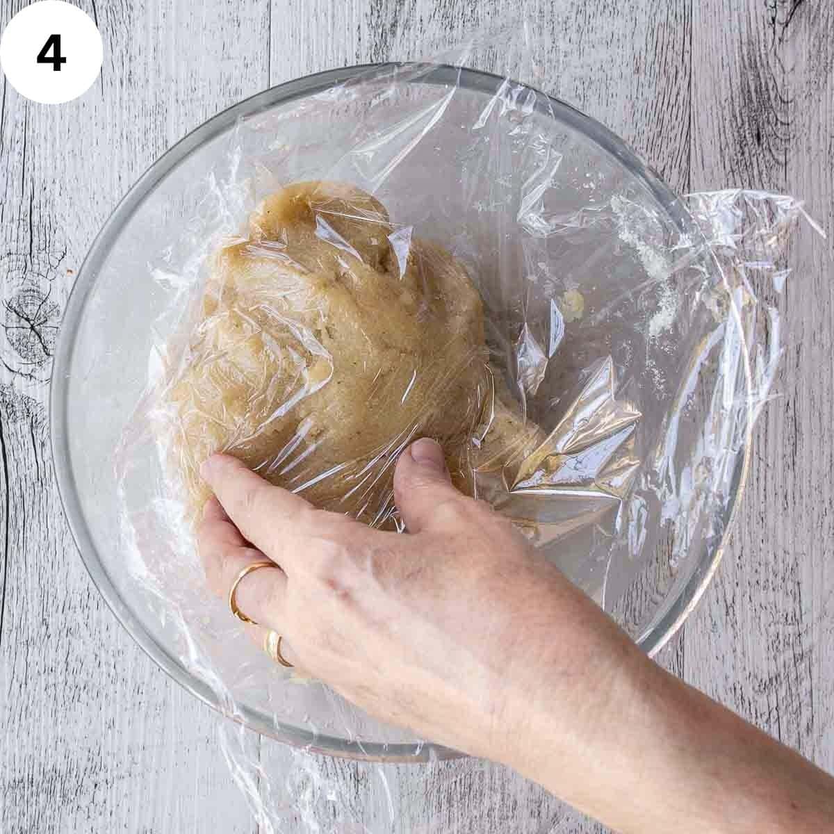 Plastic wrap being placed over dough ball.