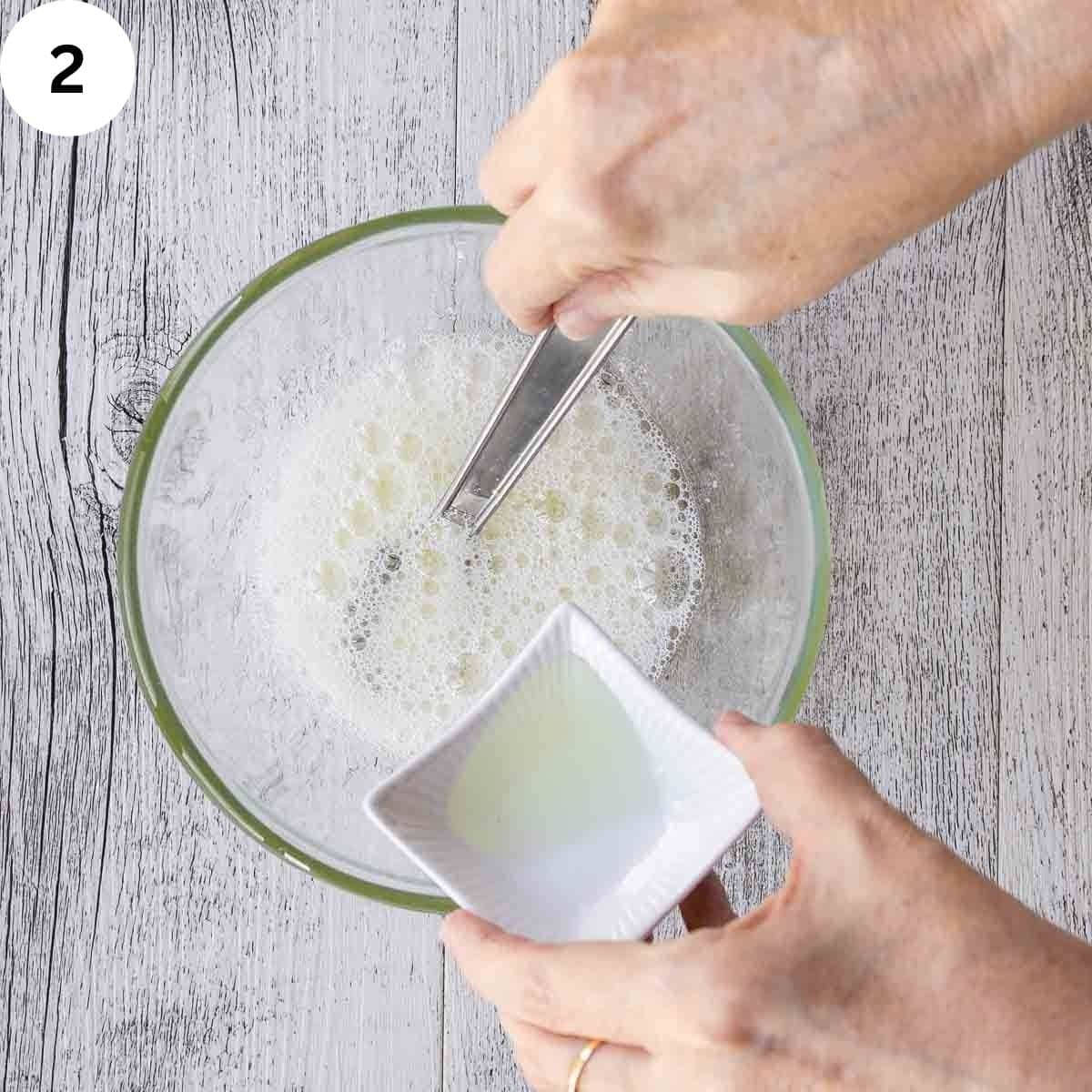Frothy egg white in a bowl; additional liquid being added.