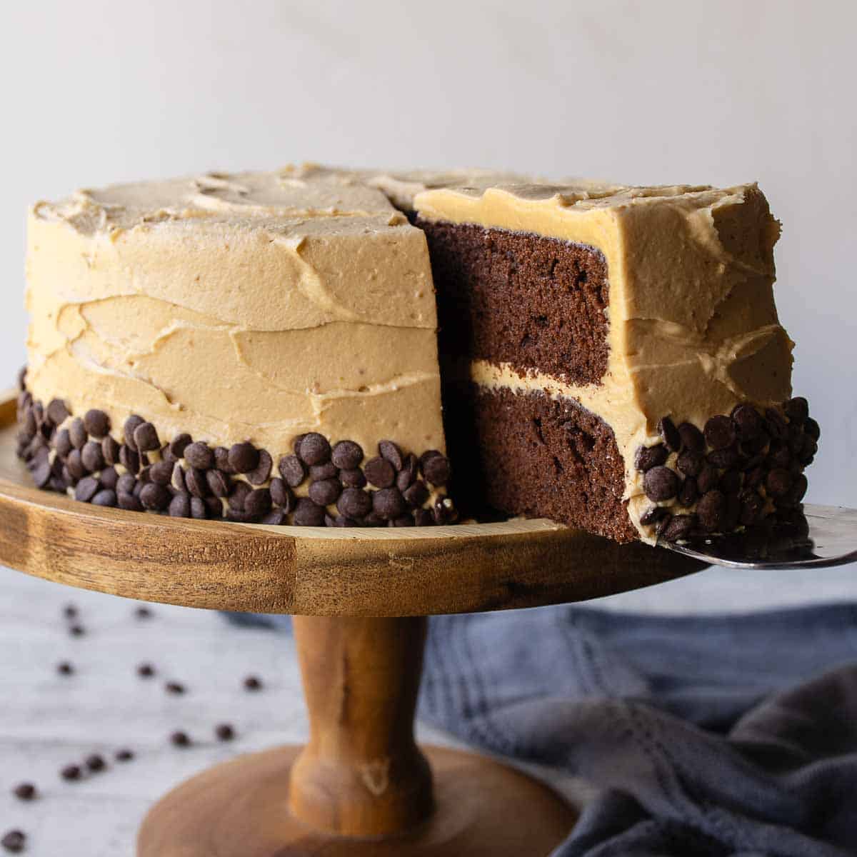 Chocolate and peanut butter cake on a wooden cake stand with a slice cut.