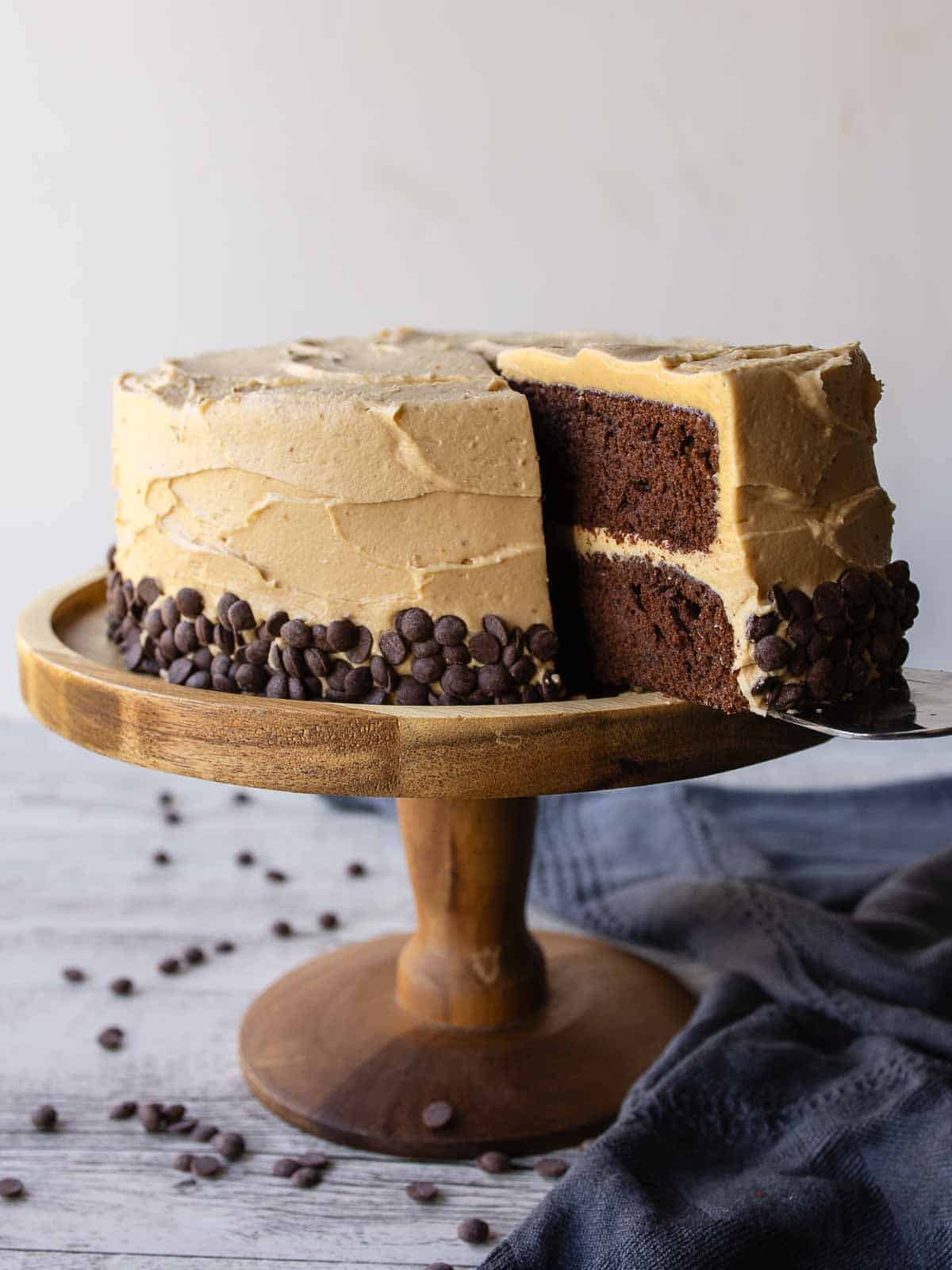 Chocolate and peanut butter cake on a wooden cake stand with a slice cut.