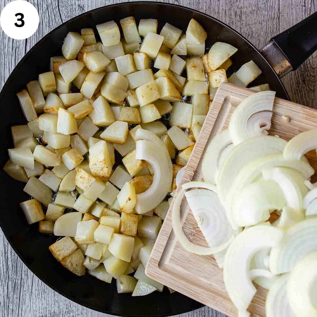 Adding sliced onions to a pan of fried potatoes.
