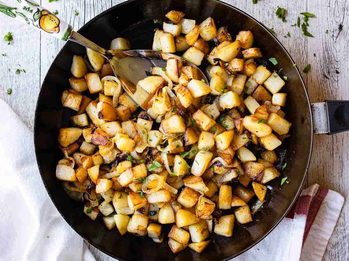 Overhead view of fried cubed potatoes in a black skillet.